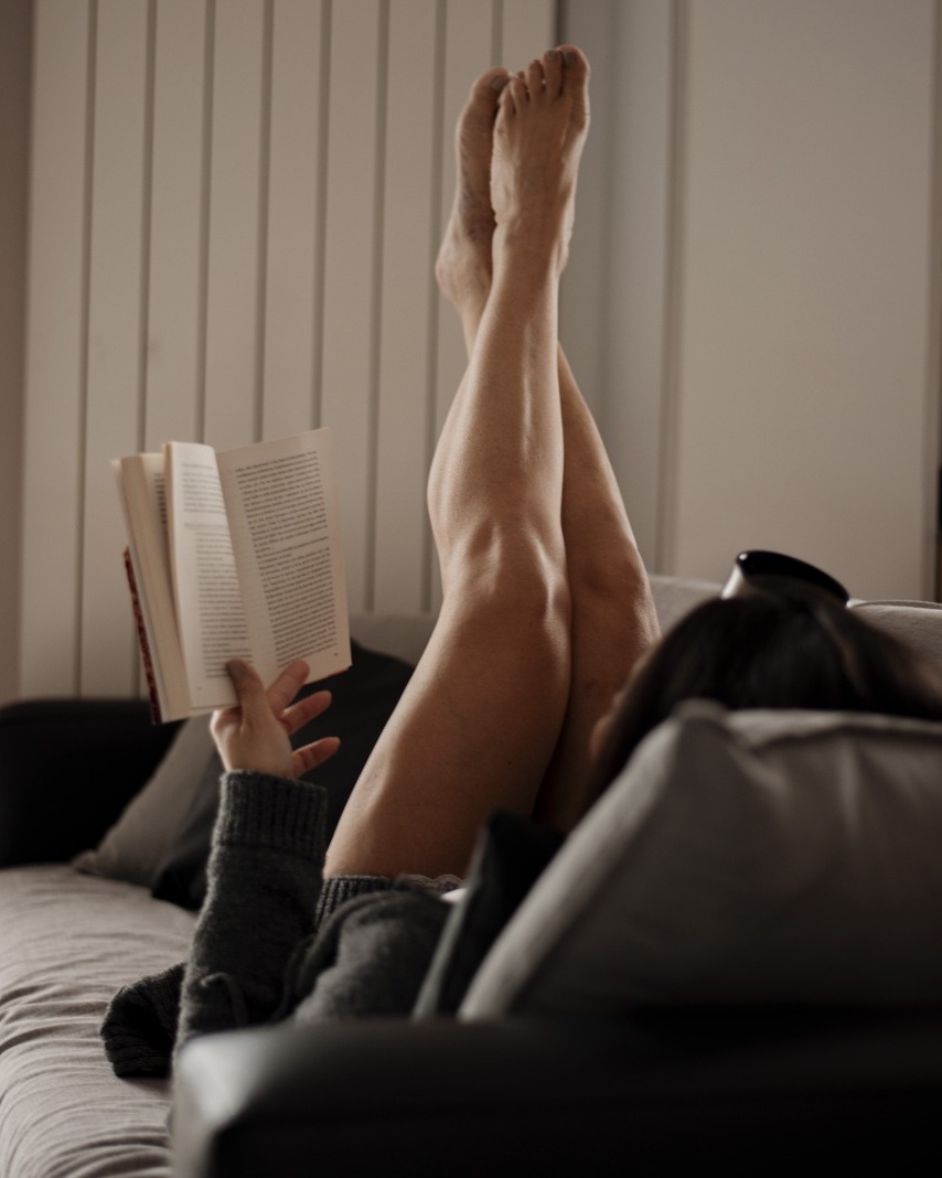 Donna con gambe sollevate sul divano a fine giornata, sensazione di gambe pesanti e gonfie nonostante l’allenamento